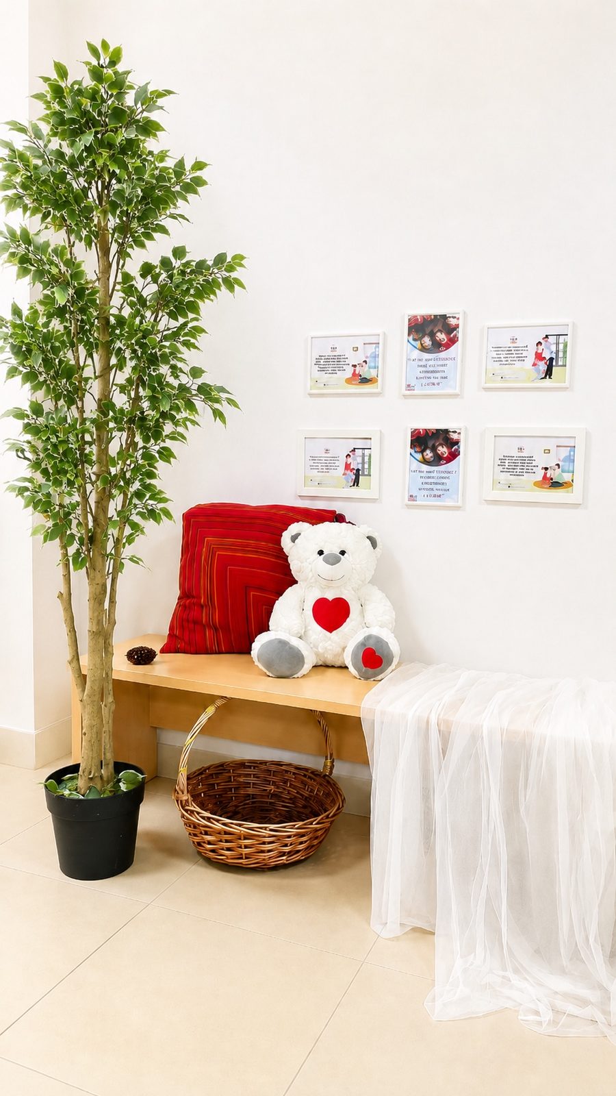 Framed prints on the wall above a bench with a large teddy bear and a potted ficus, in a corner at Mosaic