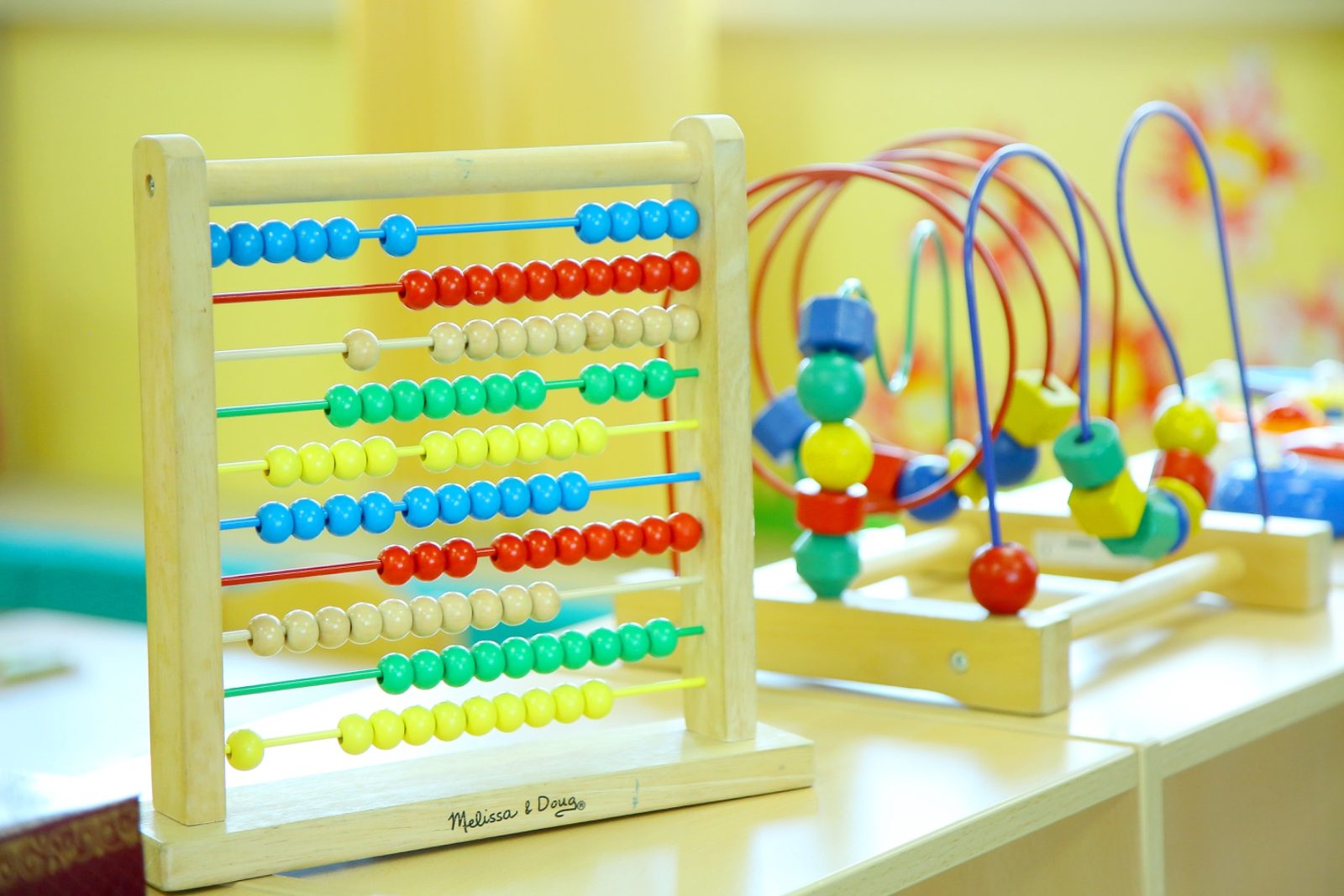 A wooden abacus and a bead-maze toy set out on a low shelf beside a window