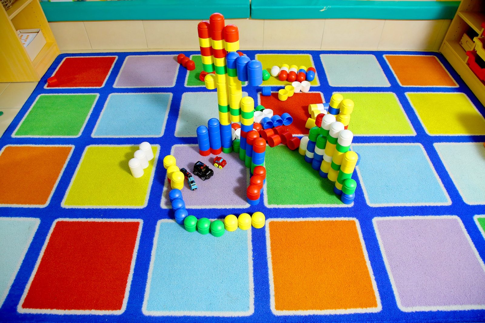 Interlocking construction blocks built into towers and walls on a large primary-coloured floor rug
